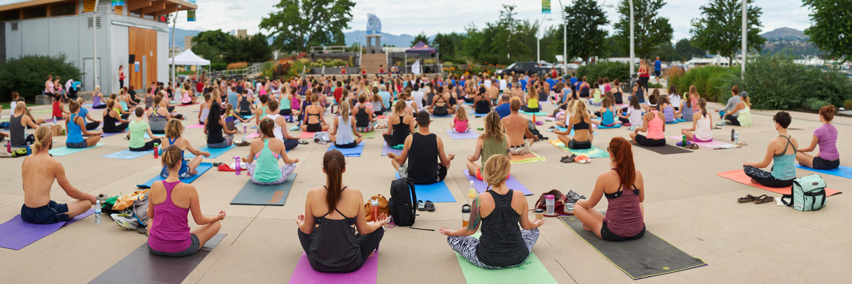 A large group of people in Stuart Park sitting cross-legged on their yoga mats on an overcast day