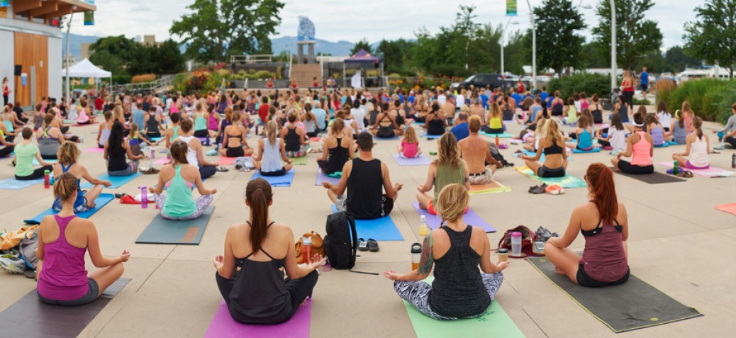 A large group of people in Stuart Park sitting cross-legged on their yoga mats on an overcast day