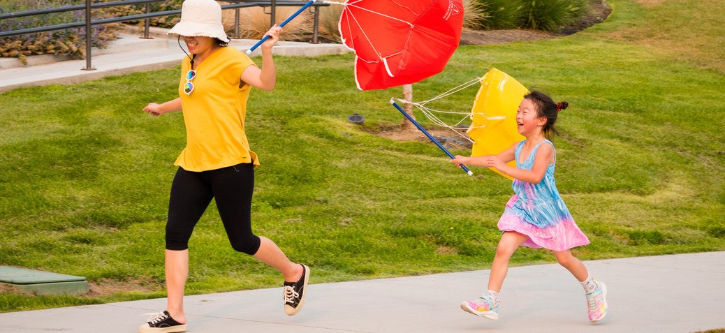 A young girl and a woman run along a path holding kites in a sunny park