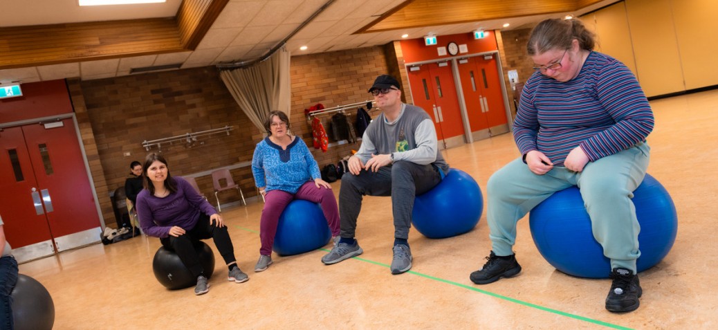 Four adults sit on big blue exercise balls during an adaptive fitness class at PRC.
