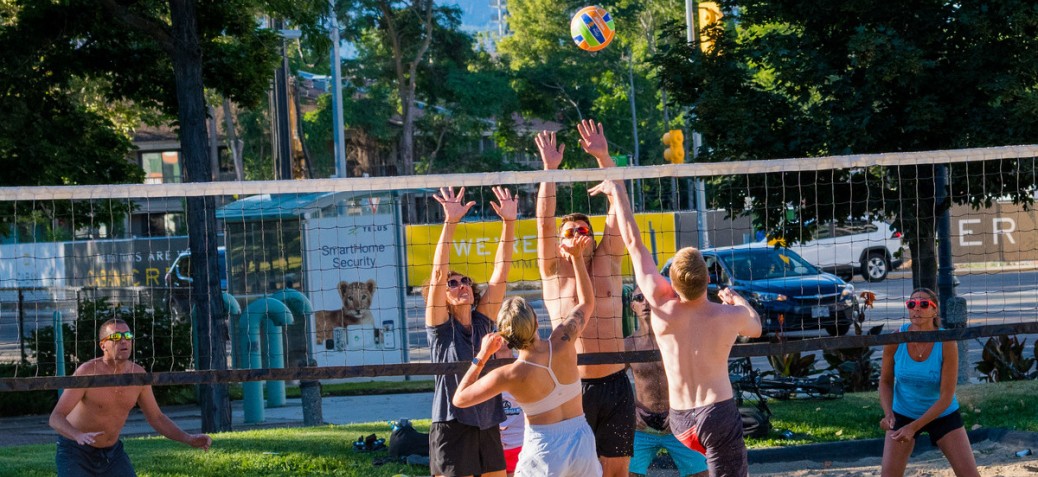 A group of young adults jumping towards the volleyball net for the ball at Gyro Beach on a sunny day.
