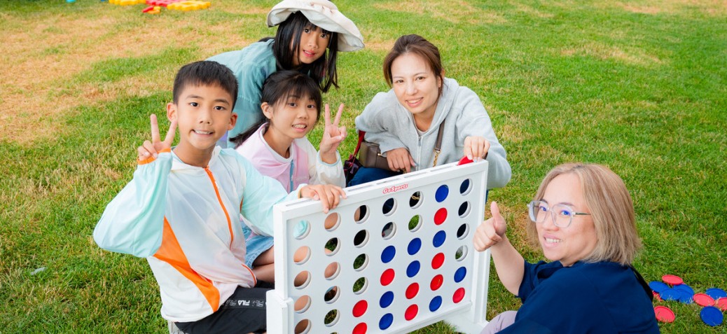 Friends playing Connect-4 A group of five friends playing giant Connect-4. They are giving a thumbs up or a peace sign and are all smiling.