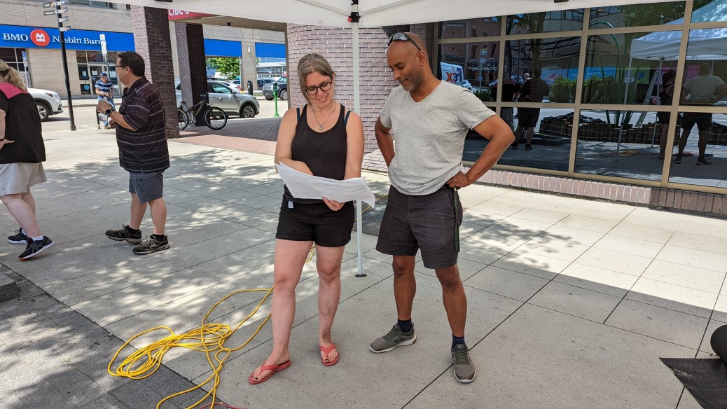 A pair of workers consult plans during the installation of a parklet on a downtown street