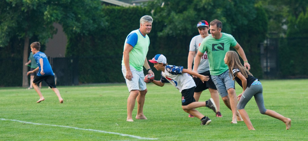 A group of children and parents play a game of touch football on a green sports field. 