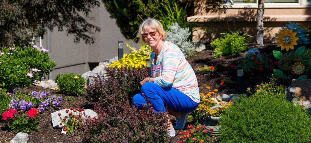 A woman in a pastel-coloured, striped shirt crouches in a garden, highlighting its water-efficient irrigation system
