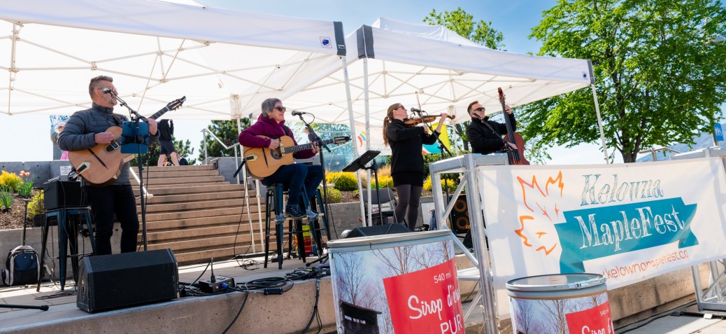 Kelowna MapleFest band on stage, blue sky and maple syrup barrels dislayed