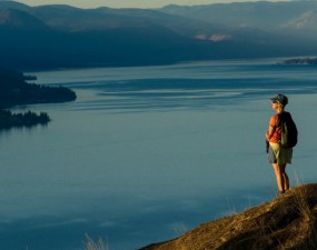 A woman hiker stands on a hill at sunset overlooking Okanagan Lake