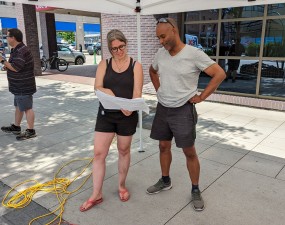 A pair of workers consult plans during the installation of a parklet on a downtown street