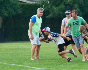 A group of children and parents play a game of touch football on a green sports field. 