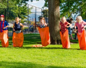 Six smiling children participating in a sack race on a sunny day.