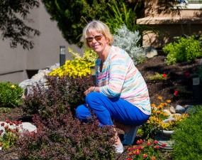 A woman in a pastel-coloured, striped shirt crouches in a garden