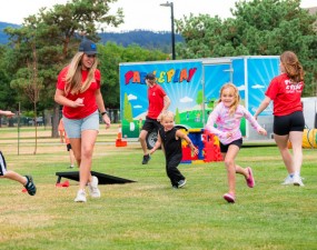 Young kids running in the grass in front of a Park & Play trailer