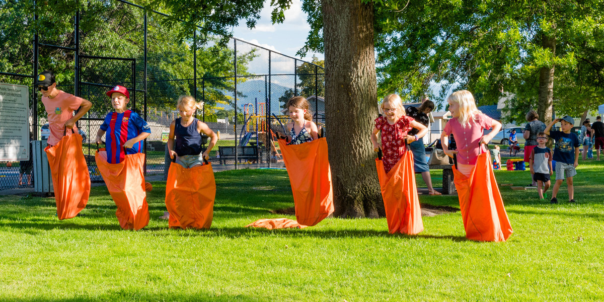 A group of six kids in orange sacks participating in a sack race on a sunny day at Hartwick Park.